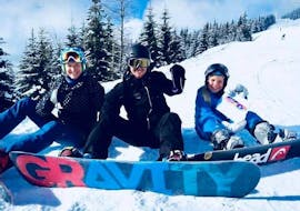 Een blije groep snowboarders zit in de sneeuw tijdens privé snowboardlessen voor kinderen en volwassenen van alle niveaus. 