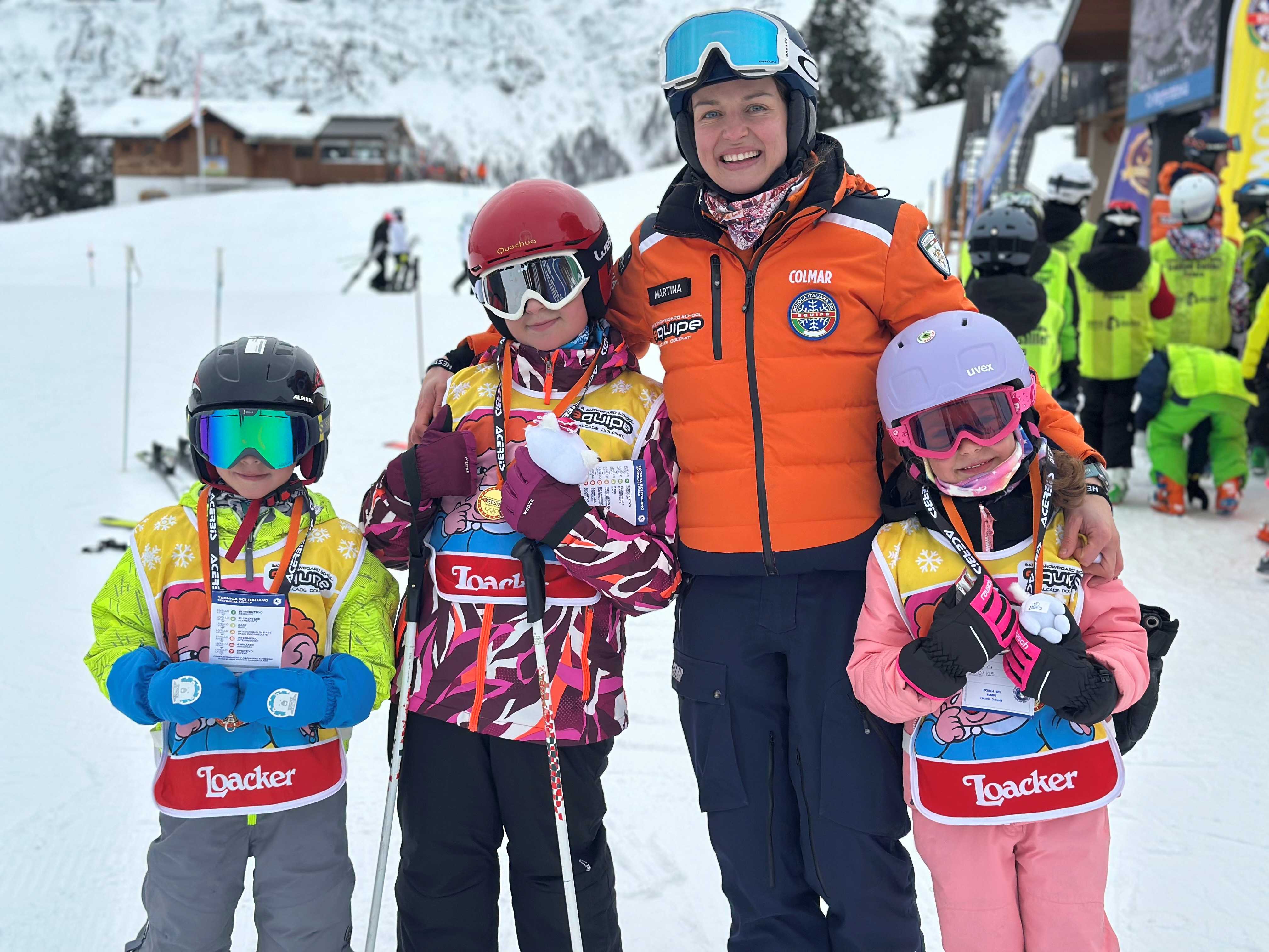 Kids and ski instructor taking a fun picture in Falcade after one of the Kids Ski Lessons "Mini Group" (4-12 y.) of All Levels.