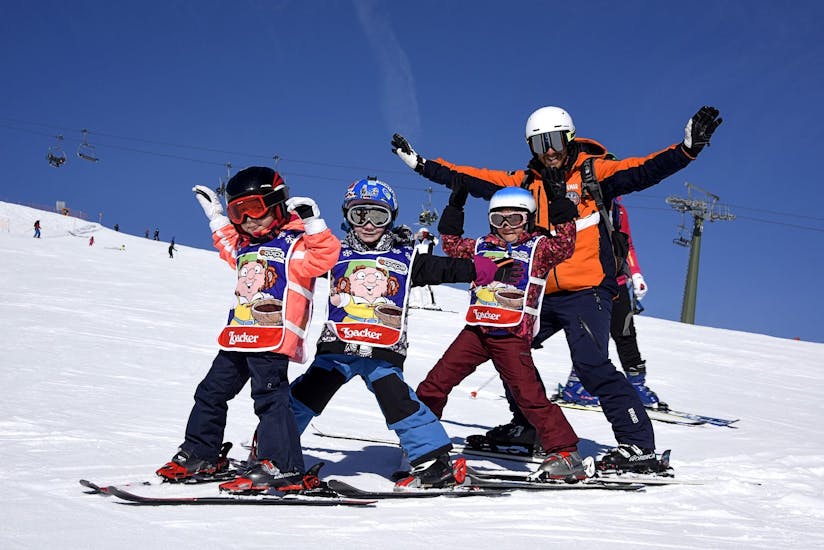 Kids and ski instructor taking a fun picture in Falcade after one of the Kids Ski Lessons "Mini Group" (4-12 y.) of All Levels.