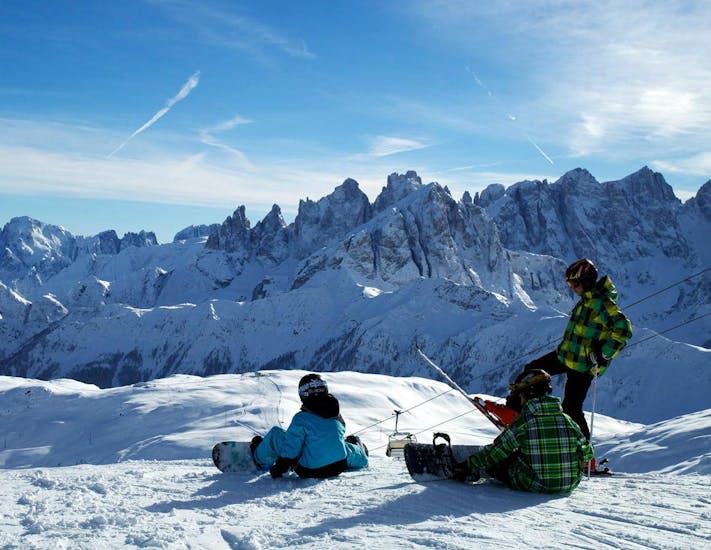 Snowboarders in front of the mountains of Falcade during one of Snowboarding Lessons for Kids & Adults of All Levels.the