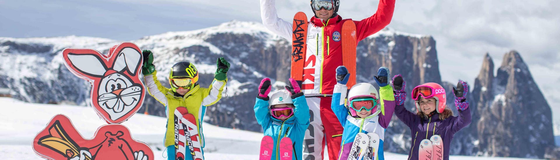 Eine Gruppe von Kindern hat Spaß im Schnee mit ihrem Skilehrer von der Skischule Seiser Alm.