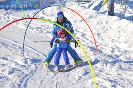 Un moniteur de ski aide un enfant à dévaler la pente pendant les cours de ski pour enfants (4-14 ans) - Demi-journée - Première fois de l'école de ski Scuola di Sci Azzurra Livigno.