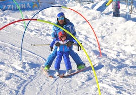 Group Kids Ski Lessons (4-14 y.) for First Timers - Half Day from Scuola di Sci Azzurra Livigno A ski instructor helps a child to ski down the slope during the Kids Ski Lessons (4-14 y.) - Half Day - First Timer of the ski school Scuola di Sci Azzurra Livigno.