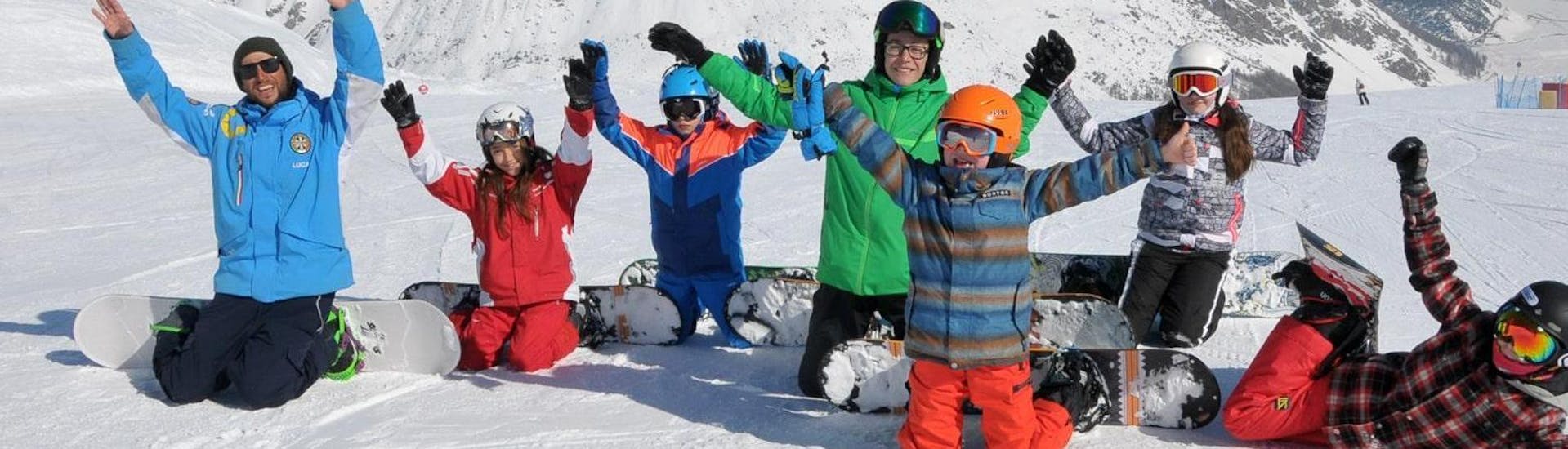 Un gruppo di bambini si diverte sulla neve con il maestro di snowboard della scuola di sci Scuola di Sci Azzurra Livigno durante le lezioni di snowboard per bambini e adulti di tutti i livelli.