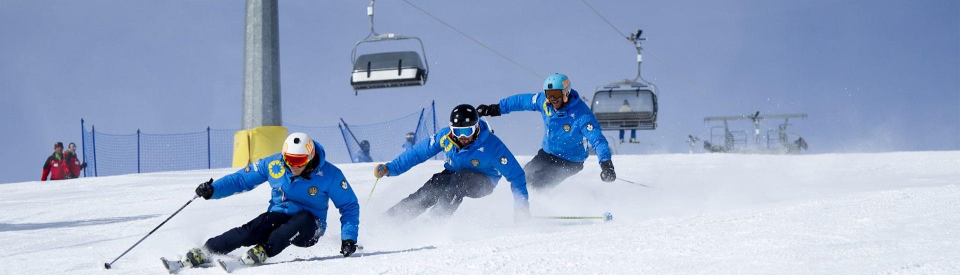 Three ski instructors from the ski school Scuola di Sci Azzurra Livigno skiing down the ski slope in formation during one of the Ski Lessons for Adults - All Levels, thereby demonstrating the right skiing technique.