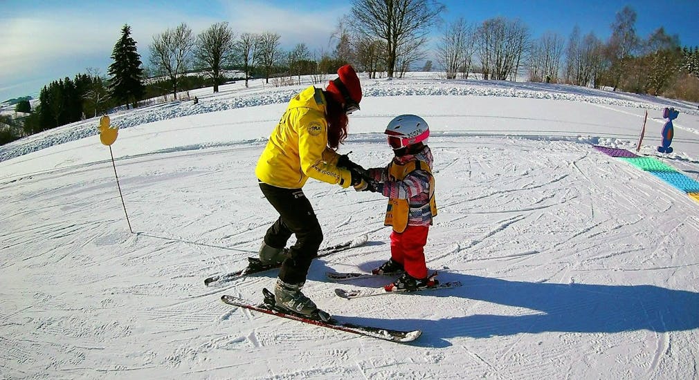 Ein Skilehrer der Skischule Yellow Point Špindlerův Mlýn bringt einem Mädchen im Rahmen des privaten Skikurses für Kinder und Jugendliche jeden Alters das Fahren mit dem Schneepflug bei.