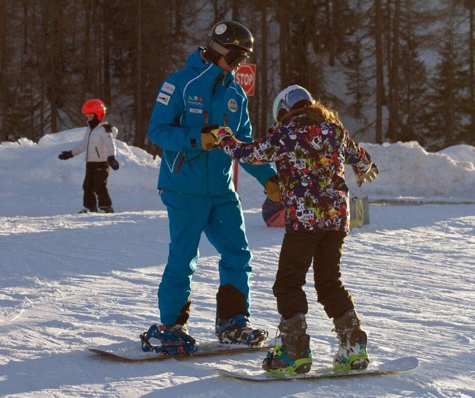 Snowboard instructor and a kid are on the slopes of Valmalenco during one of the Kids Snowboarding Lessons (6-12 y.).