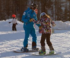 Ein Snowboardlehrer und ein Kind sind auf den Pisten von Valmalenco in einem der Kinder-Snowboardkurse (6-12 J.) unterwegs.