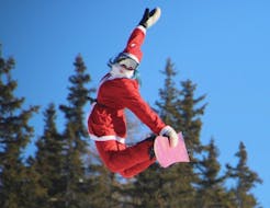 A snowboard instructor in Santa's clothing jumps in the air in Valmalenco after a Private Snowboarding Lessons for Kids & Adults of All Levels.
