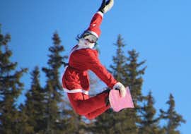 Privé snowboardlessen voor kinderen en volwassenen van alle niveaus met Enjoyski School Valmalenco Een snowboardleraar in Santa's kleding springt de lucht in in Valmalenco na een privé snowboardlessen voor kinderen en volwassenen van alle niveaus.