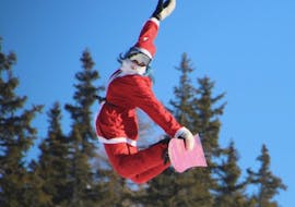 A snowboard instructor in Santa's clothing jumps in the air in Valmalenco after a Private Snowboarding Lessons for Kids & Adults of All Levels.
