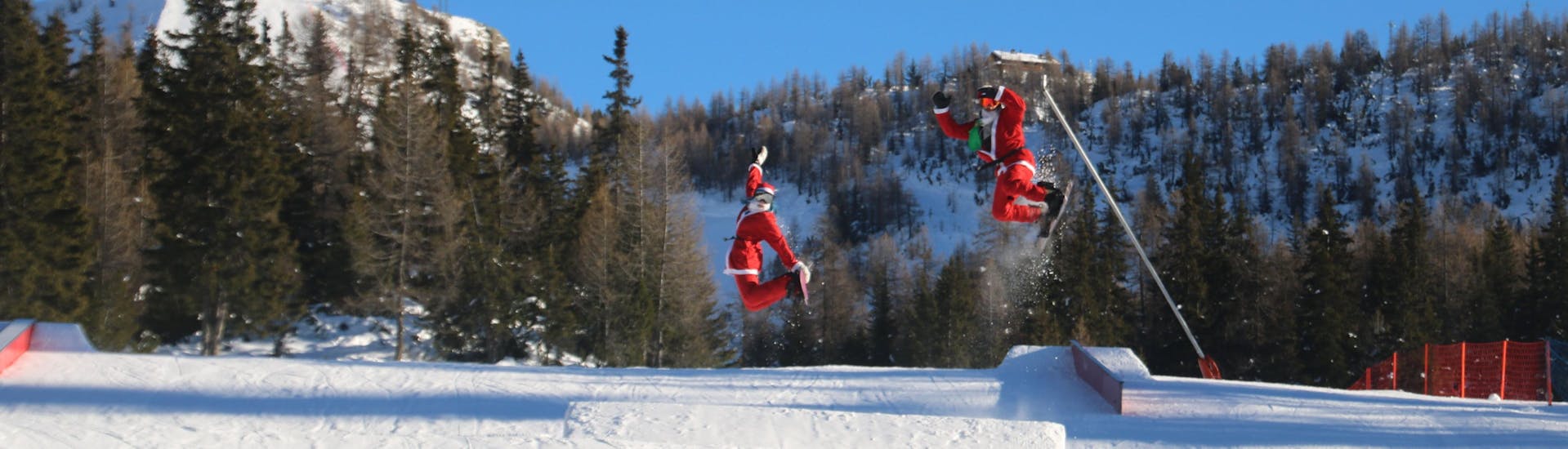 Due Babbi Natale saltano dalla gioia dopo una lezione privata di snowboard per bambini e adulti di tutti i livelli.