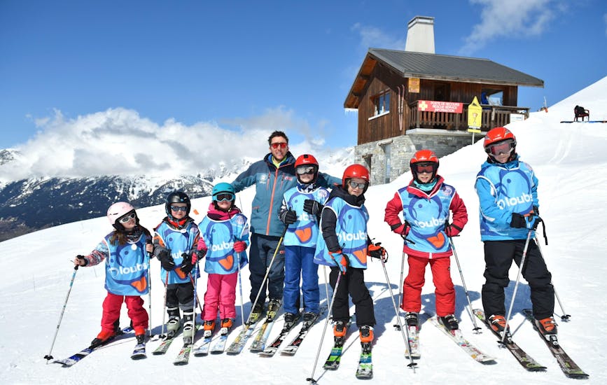 Des enfants souriants se tiennent les uns à côté des autres au sommet de la montagne pendant leur Cours de ski Enfants (5-12 ans) - Vacances - Tous niveaux avec l'école de ski ESI Valfréjus.