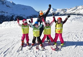 Un gruppo di sciatori è in piedi in cima alla pista con le braccia in aria con il loro maestro di sci della scuola di sci ESI Valfréjus durante le lezioni di sci per bambini (5-12 anni) - Vacanza - Tutti i livelli.