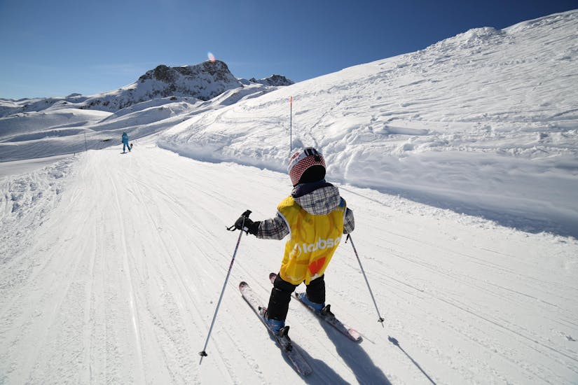 Un pequeño esquiador baja por una nevada pista de esquí durante una clase para niños (3-6 años) - Vacaciones con la escuela de esquí ESI Font Romeu.