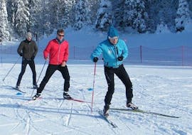 Skiers are skiing in front of a forest of snow-covered trees during their Private Cross Country Skiing Lessons - Low Season with the ski school ESI Font Romeu.