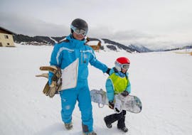 Un snowboarder camina al lado de su instructor de snowboard de la escuela de esquí ESI Font Romeu en la base de las pistas nevadas durante una clase particular de snowboard para niños y adultos - Vacaciones.